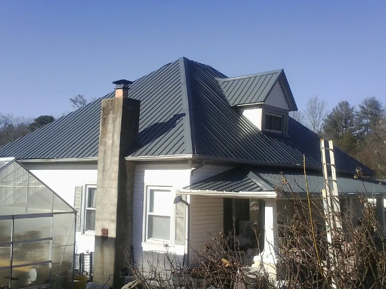 Dark blue standing seam metal roof on a white farmhouse with dormer — Slate & Tile Roof Repair by Roofing Brothers in Luebbering