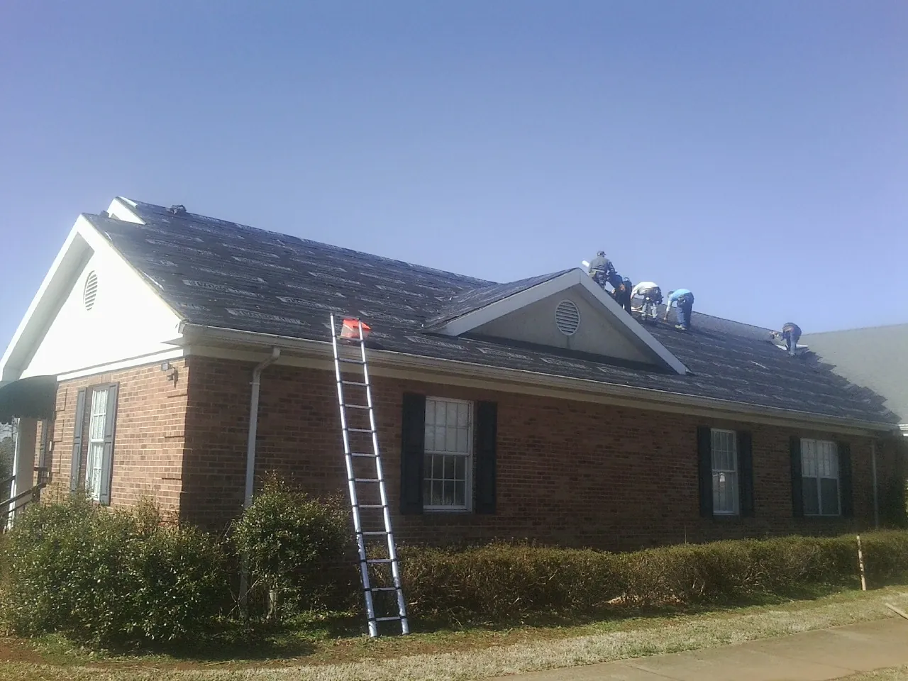 Crew tearing shingles off a brick ranch roof with a ladder set — Emergency Roof Repair work by our crew in Luebbering