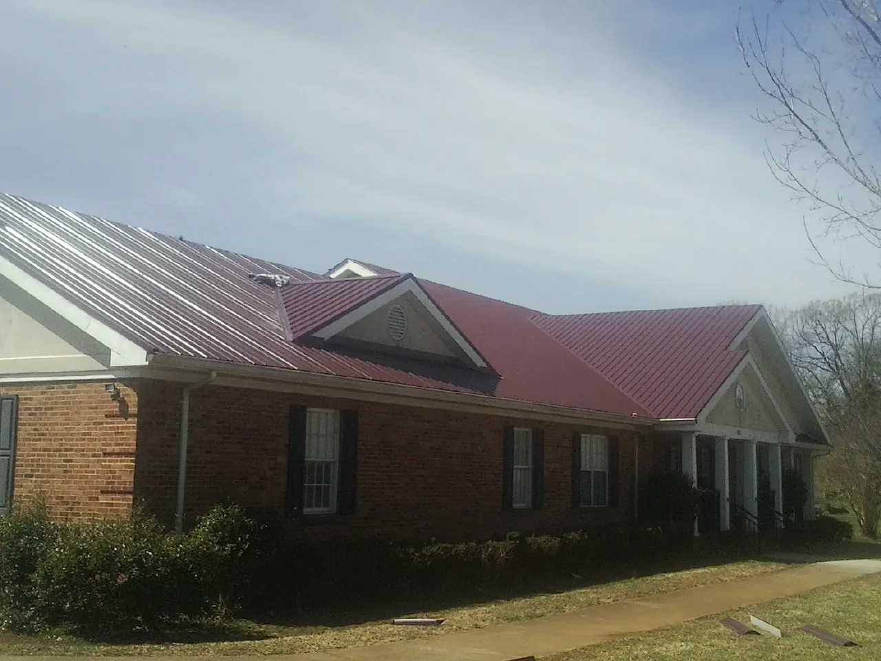 Red metal roof with gabled entries on a long brick building, from a Hail Damage Roof Repair job in Luebbering