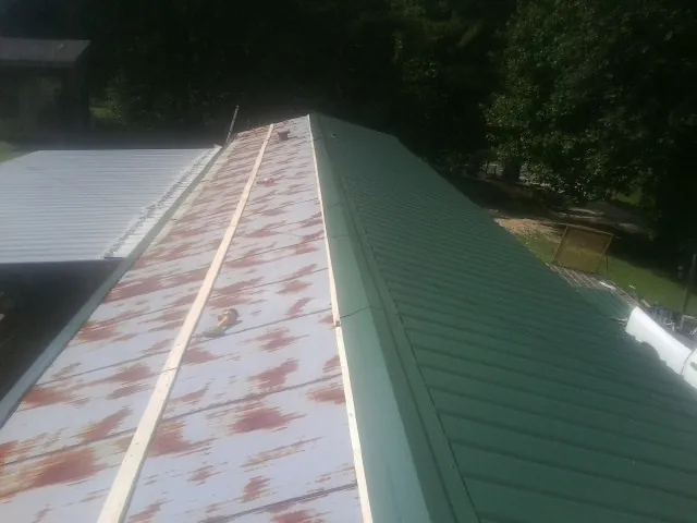 Old rusted panels beside newly installed green metal roofing — Wind Damage Roof Repair by Roofing Brothers in Luebbering