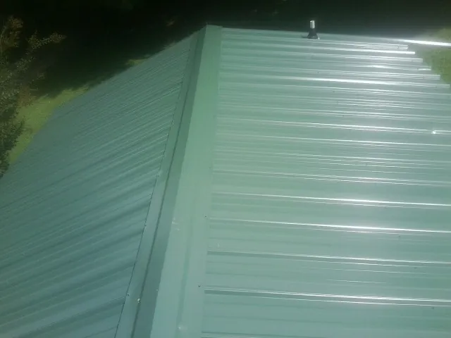New green metal panels meeting at the ridge of a roof — Flat Roof Repair work by our crew in Luebbering