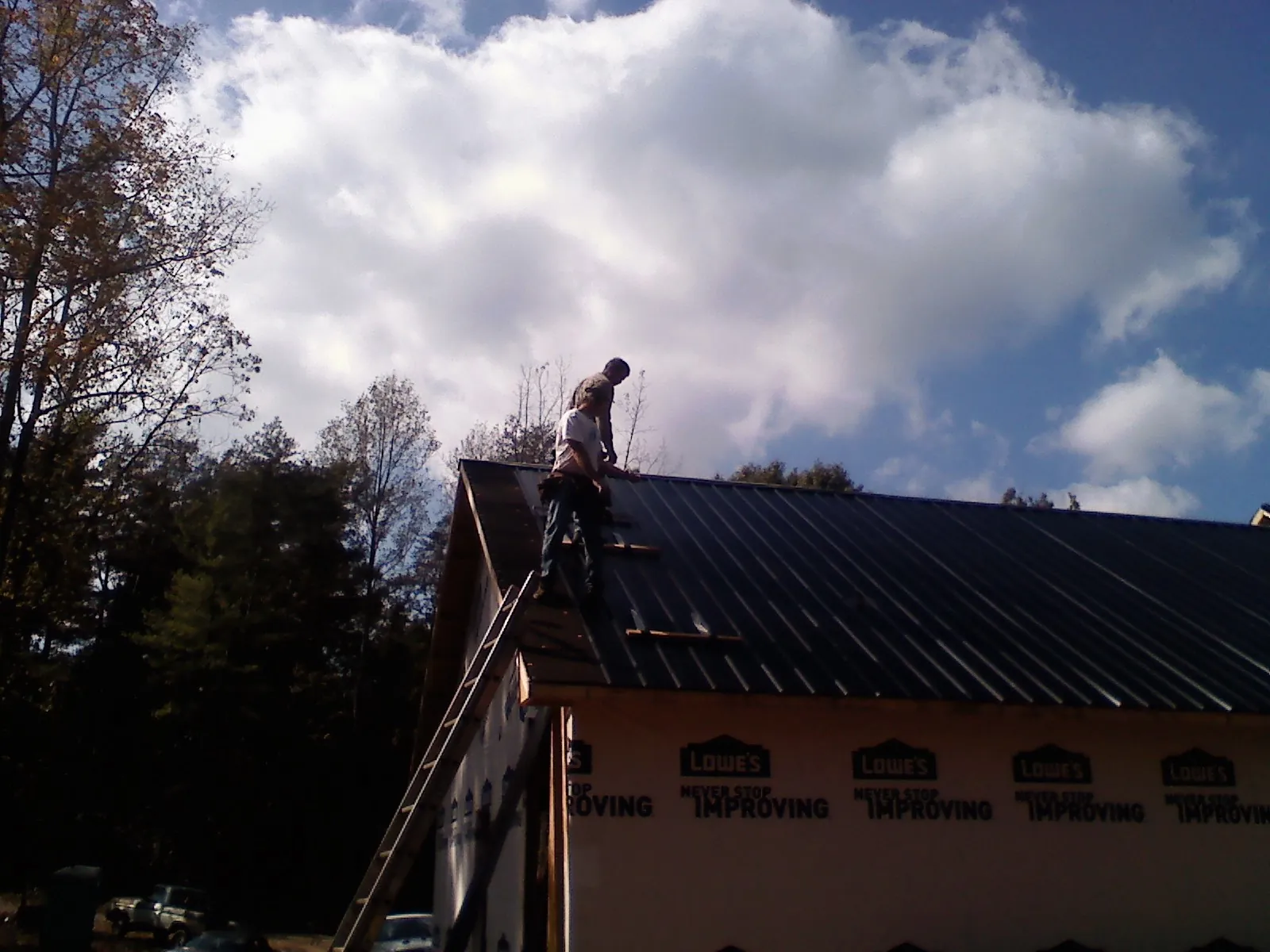 Roofer fastening dark metal panels high against a cloudy sky, from a Roof Inspection job in Luebbering