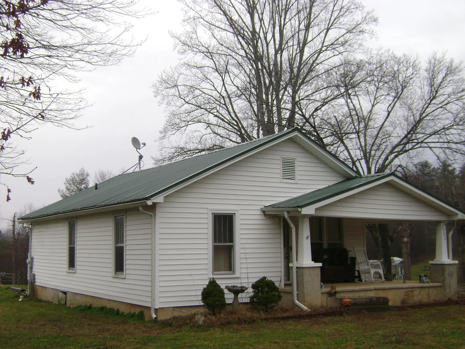 Green metal roof on a white bungalow with a side porch in Luebbering
