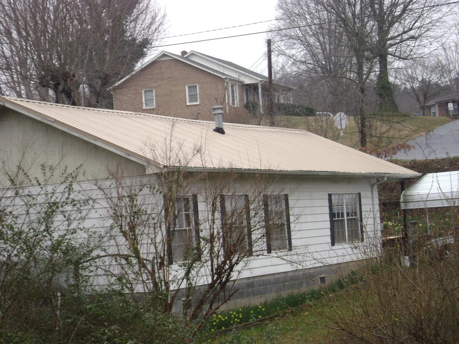 Tan metal roof on a white sided house set into a hillside — Commercial Roofing by Roofing Brothers in Luebbering