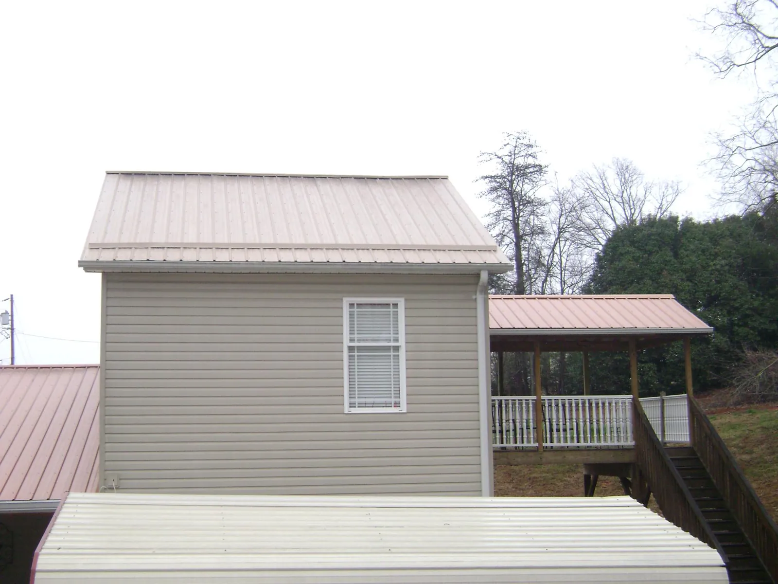 Tan metal roofs on a two story addition and attached porch, from a Roof Replacement job in Luebbering